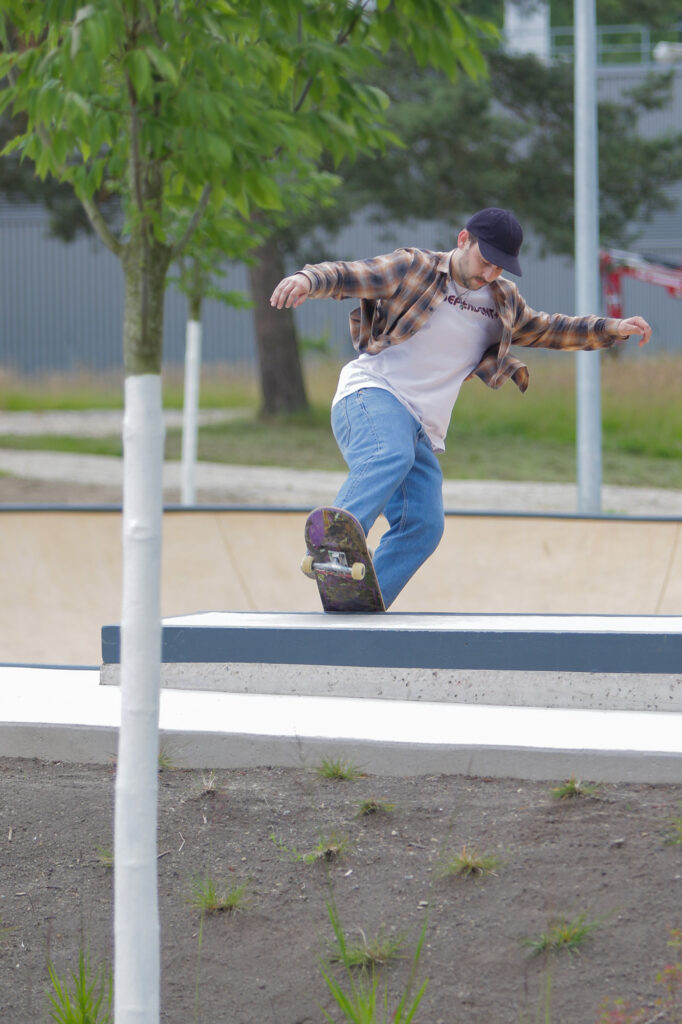 Eine Person führt einen Skateboard-Trick in einem Skate-Bowl in einer Außenumgebung aus. Die Person trägt ein kariertes Hemd, blaue Jeans und eine dunkle Kappe. Sie befindet sich mitten in einem Balance-Manöver auf dem Skateboard, das Kontakt mit der Coping des Bowls hat, was Bewegung und Geschicklichkeit in der Aktivität andeutet. Im Hintergrund sind Bäume und Gras zu sehen, was darauf hindeutet, dass es sich möglicherweise um einen Park oder einen ähnlichen Erholungsbereich handelt.

Das Bild ist interessant wegen der Darstellung von Balance und Kontrolle, die erforderlich sind, um solche Manöver auszuführen, was von Enthusiasten des Sports oder denen, die sich für dynamische Fotografie interessieren, die Bewegung einfängt, geschätzt werden kann.