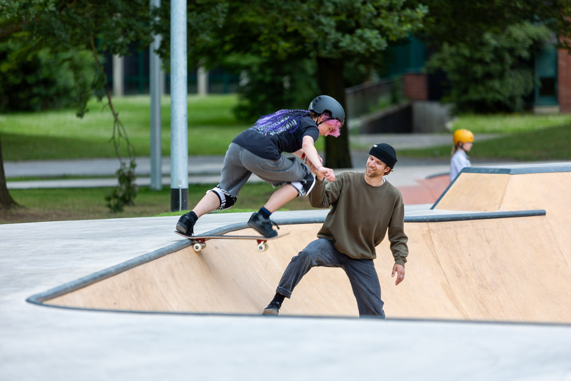 Skateboardtrainer hilft einer Kursteilnehmerin beim Drop-In